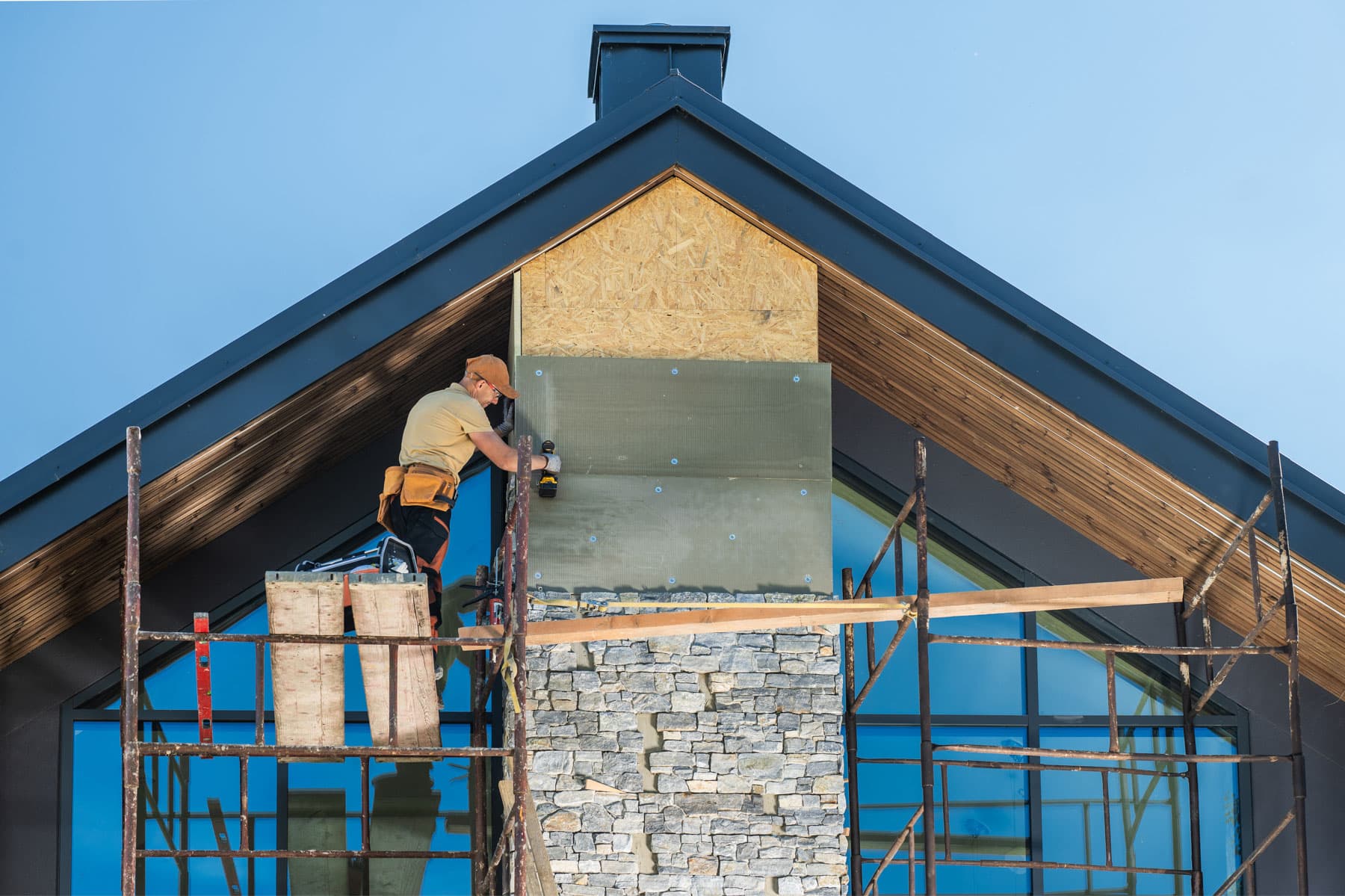 Mason installing stone veneer on a house exterior with scaffolding
